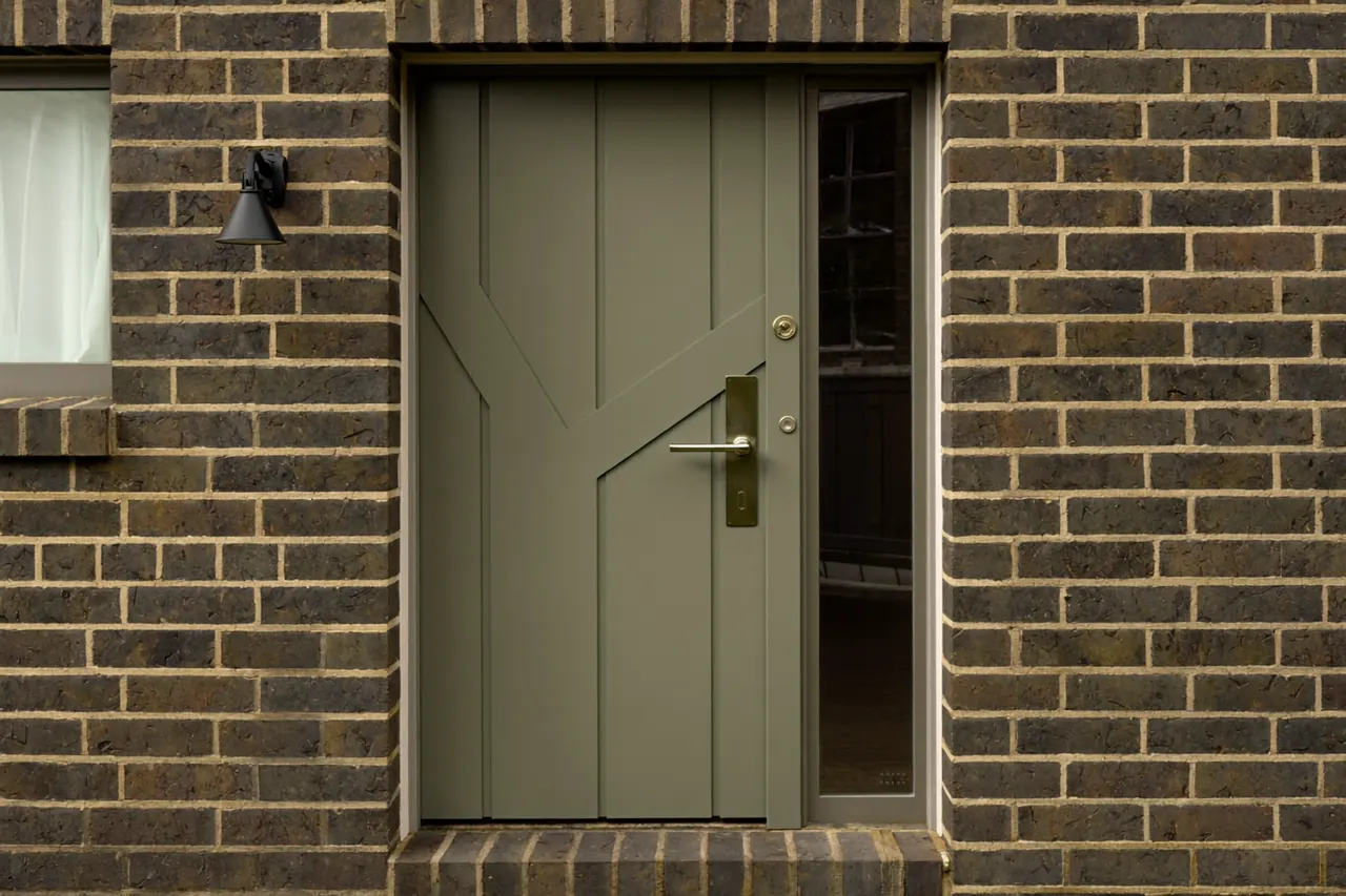 Sage-green composite front door with brushed hardware and a glazed side panel on a brick house